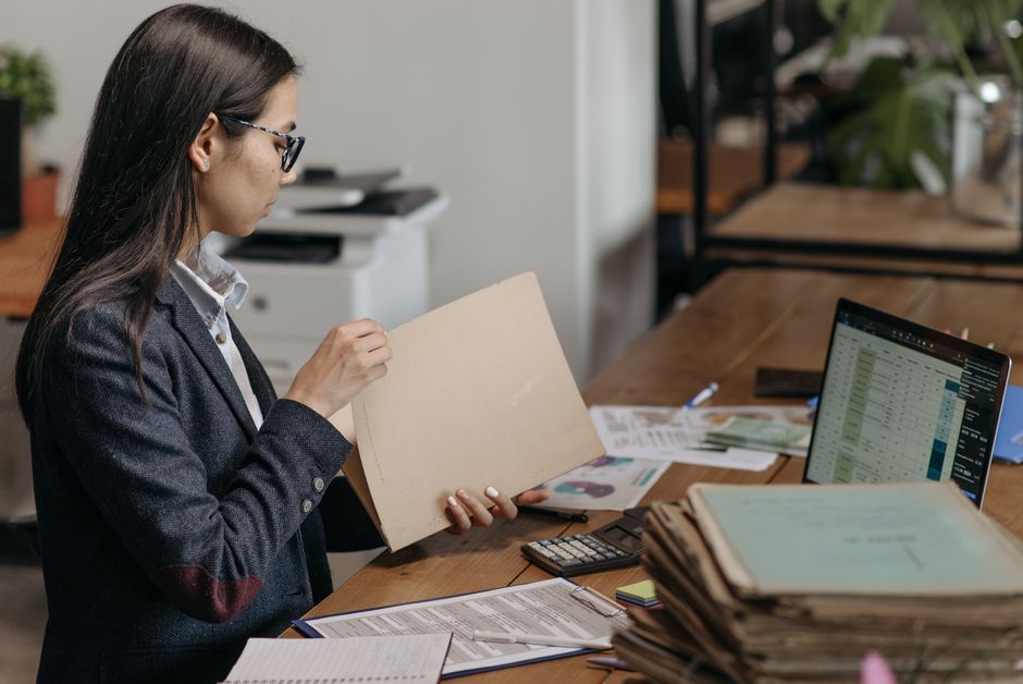 A professional woman reviewing documents at her office desk with a laptop and files.
